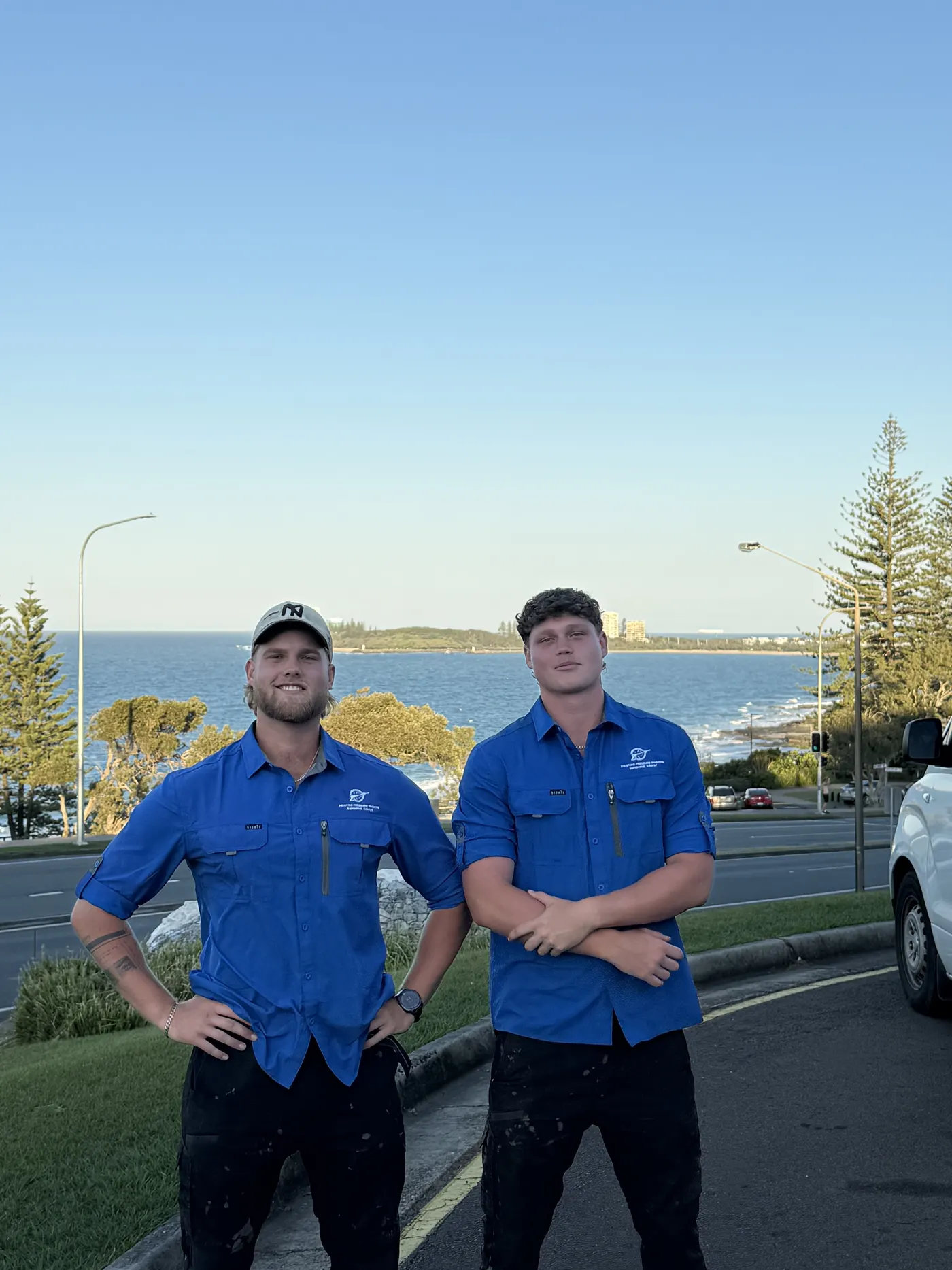 Nick and Matt from Pristine Pressure Washing in blue work shirts with the Sunshine Coast ocean behind them