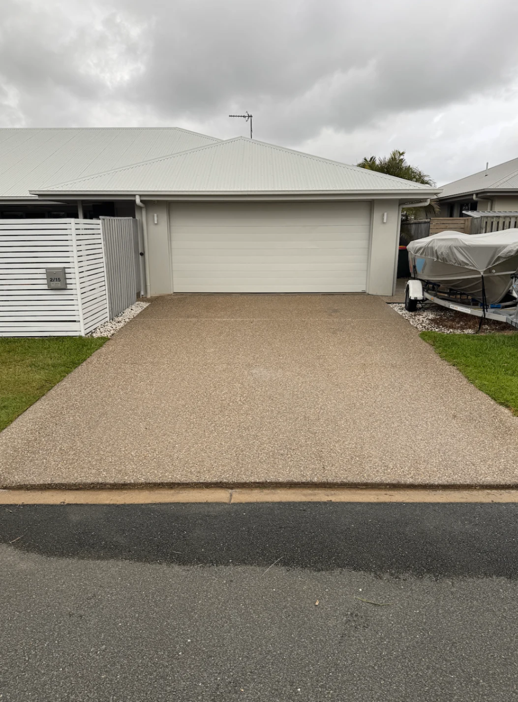 Freshly washed exposed aggregate driveway beside a boat trailer